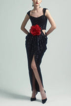 Woman wearing a black sequined gown with a red floral applique and a thigh-high slit.
