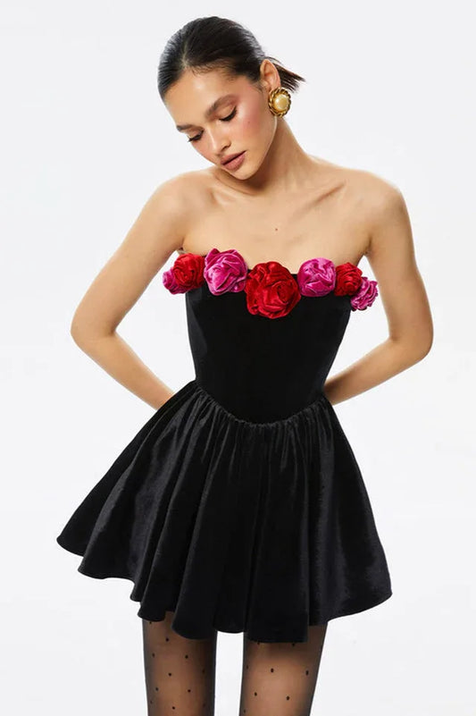 Model wearing a black velvet strapless mini dress with floral embellishments at the neckline.