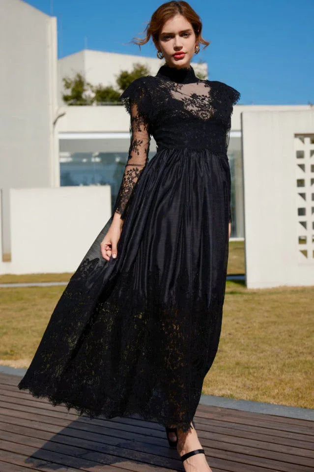 Woman in a flowing black lace and satin formal dress with her hand on her hip.