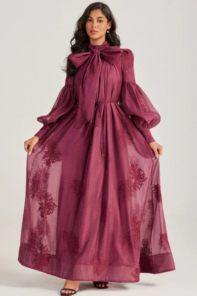 Woman displaying the full length of a long, deep purple dress with an embroidered floral pattern.