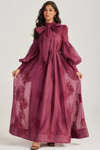 Woman displaying the full length of a long, deep purple dress with an embroidered floral pattern.