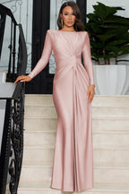 Woman in a long-sleeved, dusty rose satin gown with ruching detail standing on a staircase.