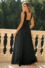 Back view of a woman in a black formal dress with a criss-cross halter neckline and flowing skirt.