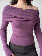 Woman wearing a purple off-the-shoulder knit top with a draped neckline and long sleeves, arms crossed.