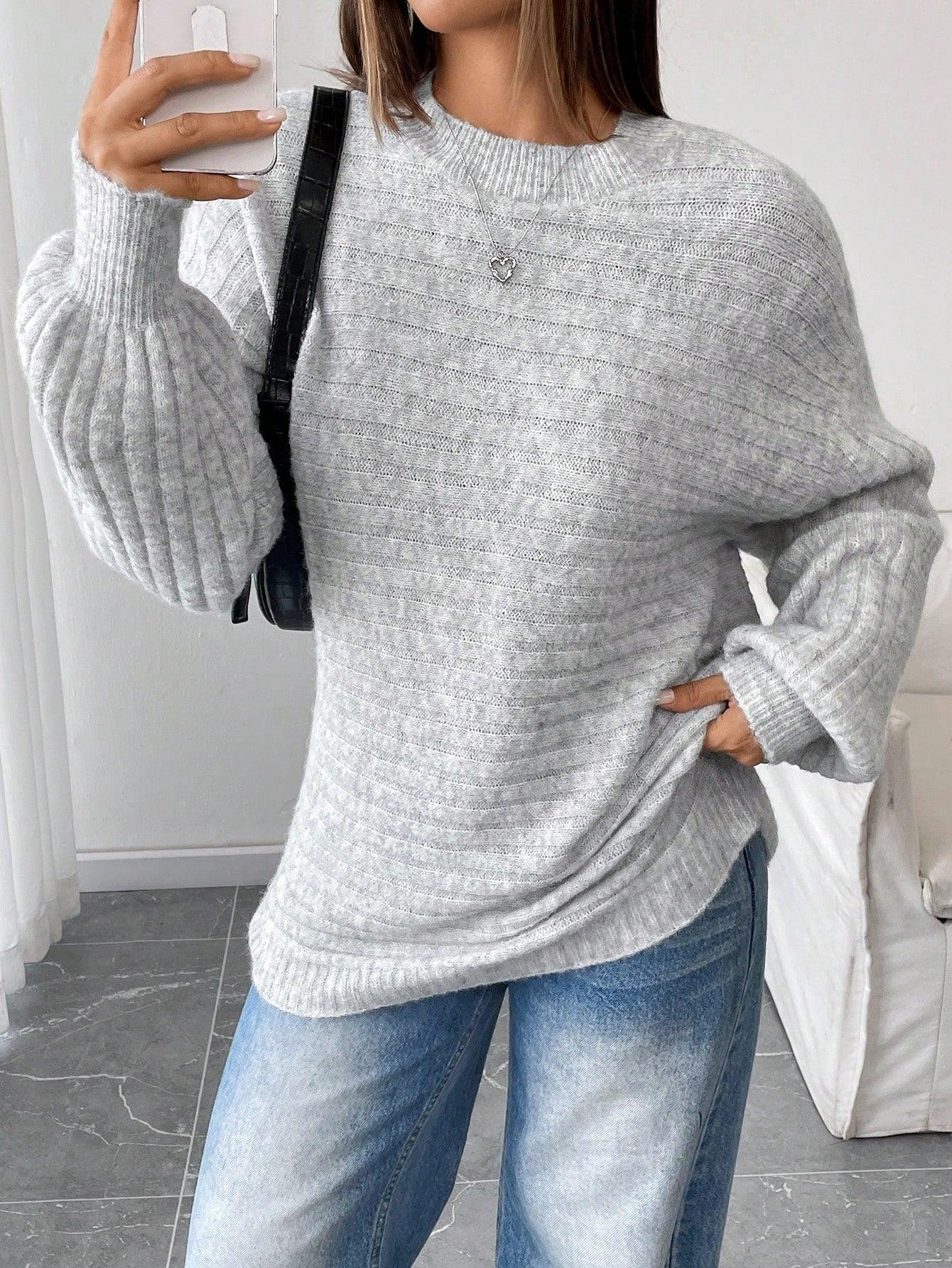 Woman taking a selfie while wearing a light grey oversized knit sweater with balloon sleeves and a crew neck, paired with blue denim jeans and a black handbag.