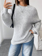 Woman taking a selfie while wearing a light grey oversized knit sweater with balloon sleeves and a crew neck, paired with blue denim jeans and a black handbag.