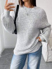 Woman taking a selfie while wearing a light grey oversized knit sweater with balloon sleeves and a crew neck, paired with blue denim jeans and a black handbag.