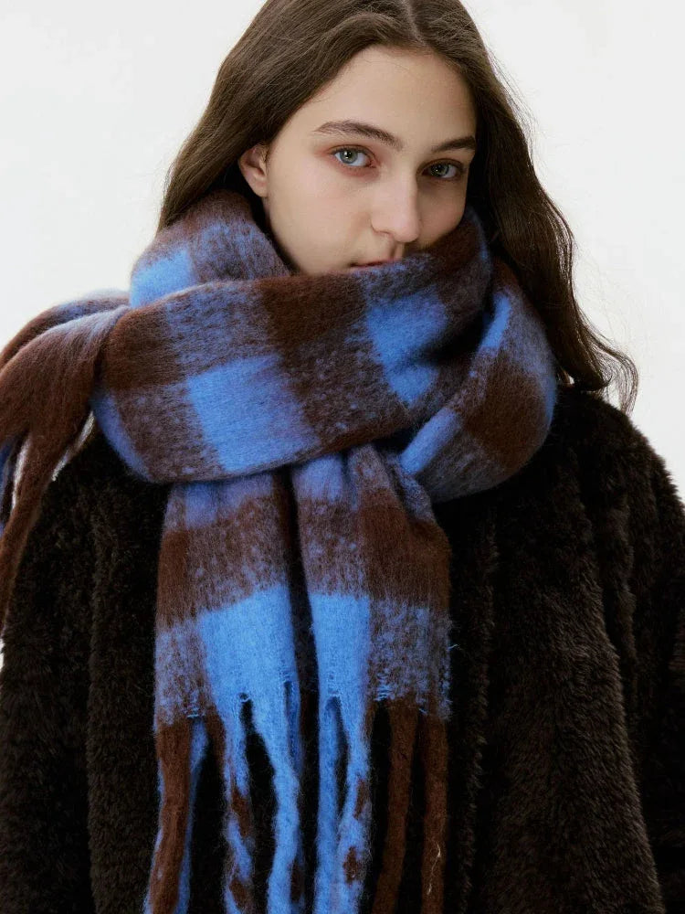 A woman's face is partially obscured by a large, oversized blue and brown plaid scarf with fringe.