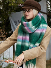 Model wearing a tan coat and a green plaid scarf with cream, pink, and blue stripes. She is also wearing a brown flat cap and round glasses, turning her head to the side.