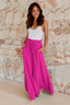 Woman wearing a white tank top and bright pink wide-leg palazzo pants standing against a stone wall.