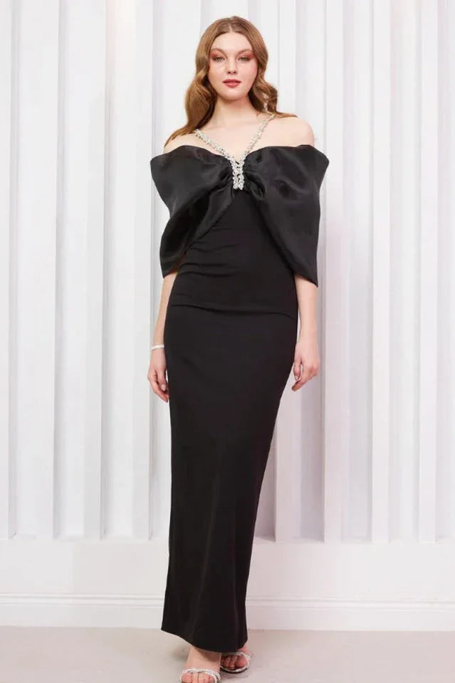 Model posing in an elegant black floor-length dress with an off-the-shoulder bow design