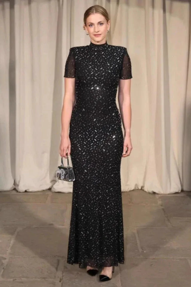 Woman in a black sequined gown with short sleeves and a high neckline, holding a silver clutch. Main image