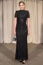 Woman in a black sequined gown with short sleeves and a high neckline, holding a silver clutch.