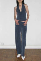 Full body shot of a woman wearing a dark blue halter neck crop top and dark blue wide leg pants, with white pointed-toe shoes.