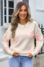 Woman wearing a cream-colored knit sweater with a pink floral print and blue jeans.