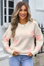 Woman wearing a cream-colored knit sweater with a pink floral print and blue jeans.