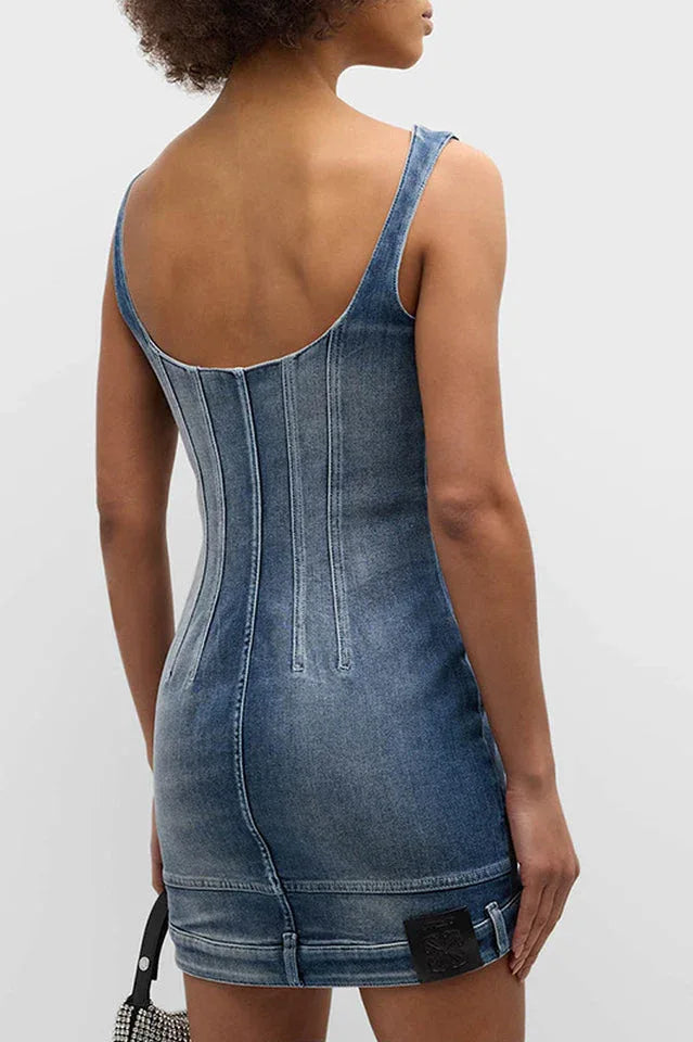 Model wearing a blue denim corset mini dress, viewed from the back, showing the open back design.