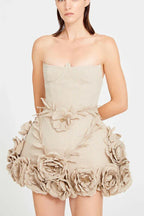 Front view of a woman in a strapless beige mini dress with a sweetheart neckline and corset detailing on the bodice. The skirt is embellished with numerous fabric flowers and leaf appliqué.