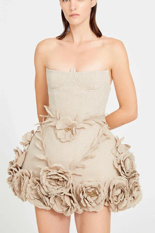 Front view of a woman in a strapless beige mini dress with a sweetheart neckline and corset detailing on the bodice. The skirt is embellished with numerous fabric flowers and leaf appliqué.