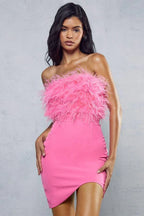Woman wearing a pink strapless dress with feather trim on the bodice and an asymmetrical hem.