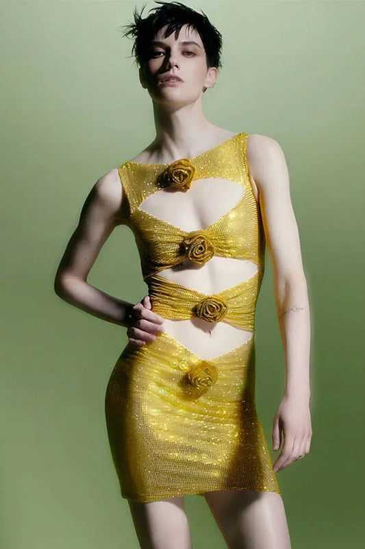 Model with short hair wearing a gold metallic knit mini dress with cut-out details and floral appliqués, side view