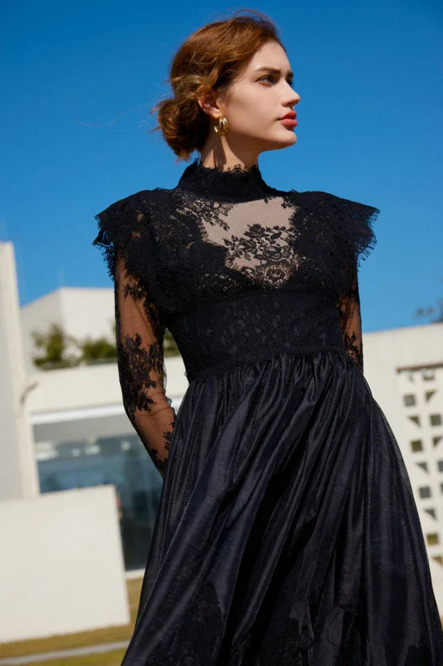 Woman posing in a black lace and satin formal dress with a high neckline and long sleeves.