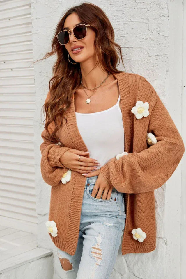 Woman wearing a brown floral cardigan over a white tank top and ripped jeans, accessorized with sunglasses and necklaces.