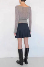Back view of a woman wearing a grey long-sleeved top, a black pleated mini skirt, and black knee-high boots.