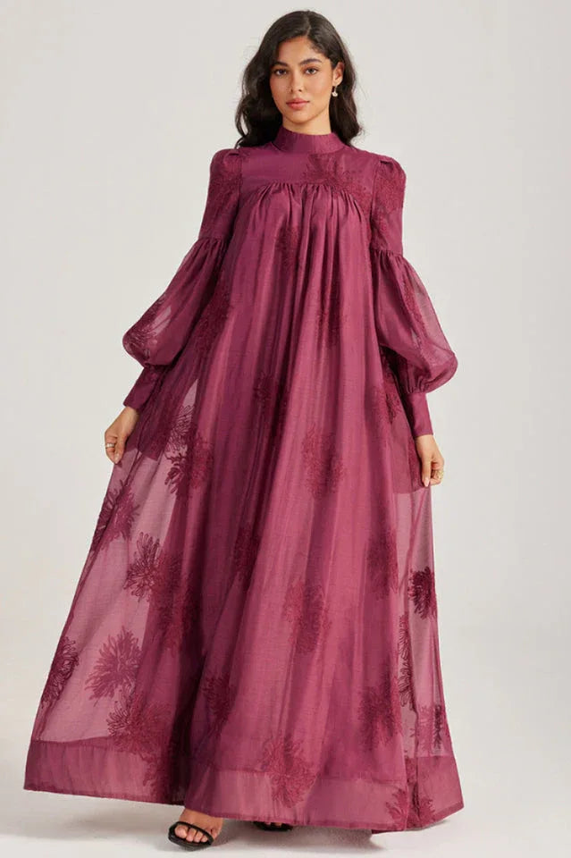 Woman showcasing the flowing skirt of a long, deep purple dress with an embroidered floral pattern.