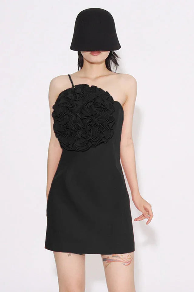 Black one-shoulder mini dress with ruffled floral applique on the bust, worn by a woman with a black bucket hat.