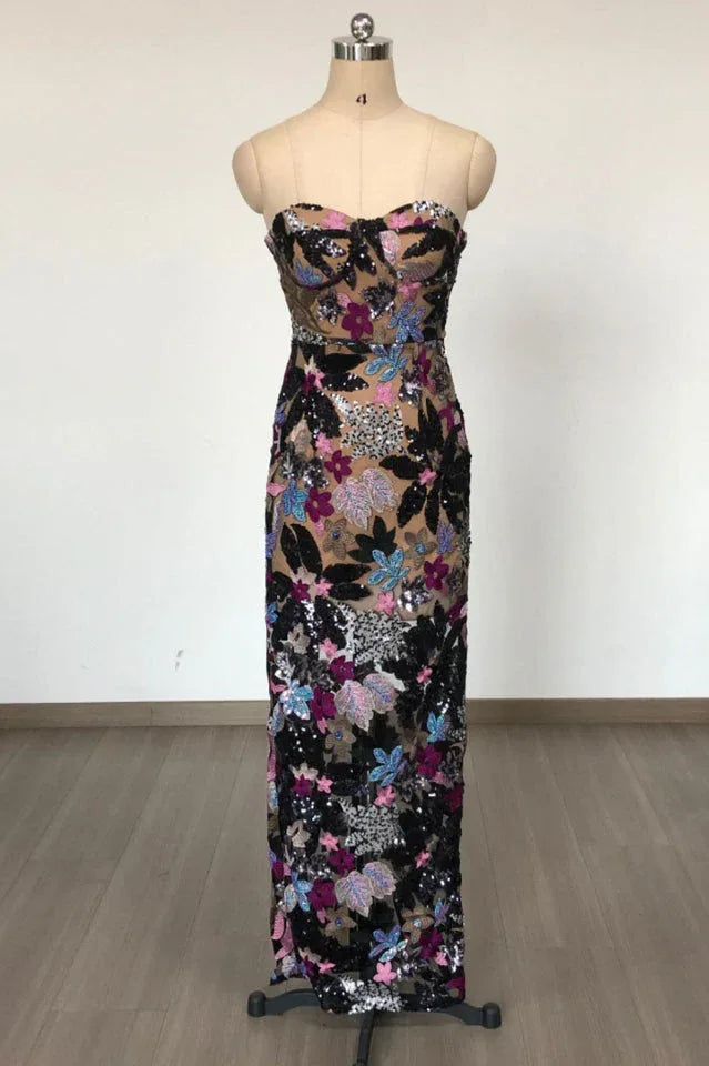 A strapless, floor-length column dress with a sweetheart neckline displayed on a mannequin. The dress is embellished with colorful floral appliques and sequins.