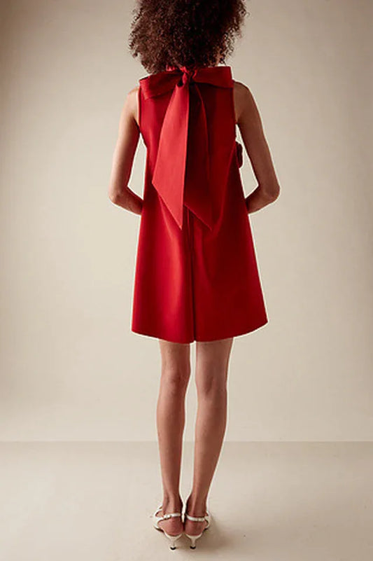 Back view of a red sleeveless A-line mini dress with a large red bow detail on the back, worn by a model.