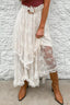 A woman wearing a white lace tiered ruffle skirt with brown boots and a brown belt.