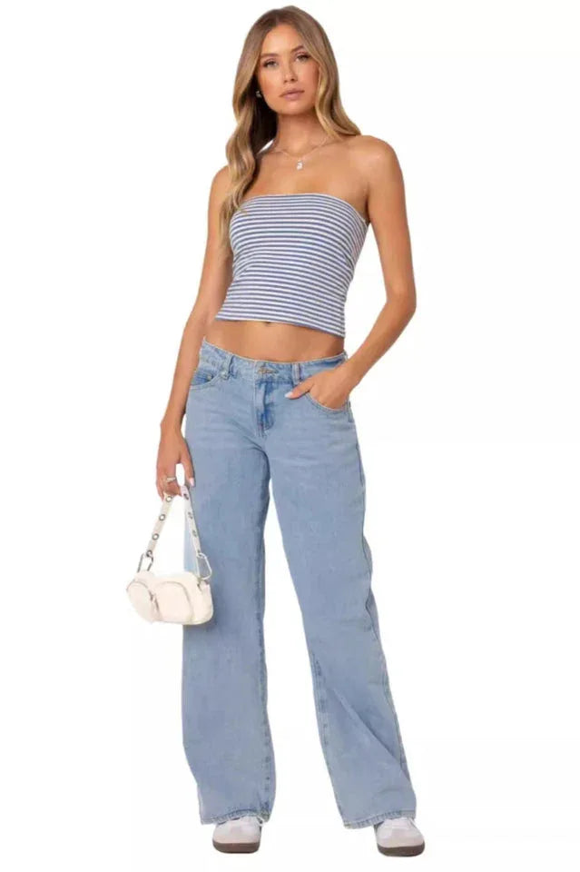 Woman wearing a blue and white striped tube top and light wash wide leg jeans, holding a white handbag