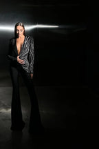 Model standing in a dimly lit setting, wearing a black jumpsuit with a striking sequin design.