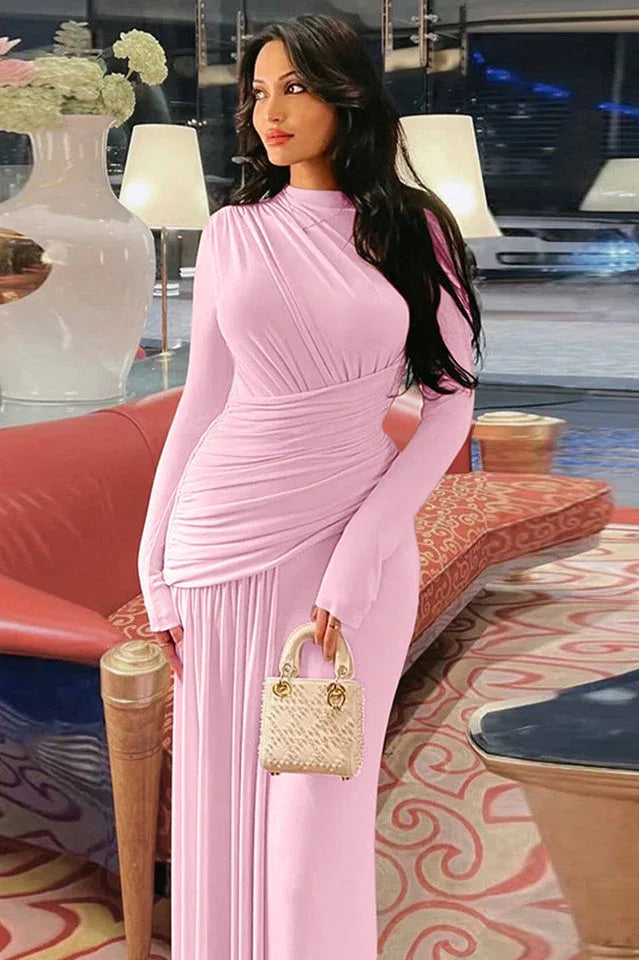 Woman in a long pink ruched dress holding a beige handbag.