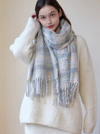 A young woman adjusts her plaid scarf while wearing a white sweater.