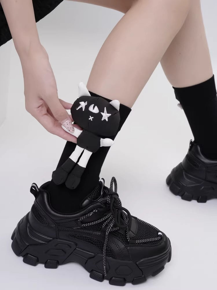 A person is holding a black sock with a cat applique on it, with black platform shoes in the foreground.