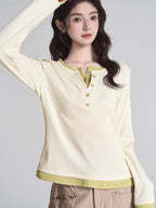 Woman wearing a cream long-sleeved shirt with green trim and buttons, paired with khaki pants.