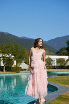 Woman in a light pink tiered tulle dress standing on the edge of a pool with mountains in the background.