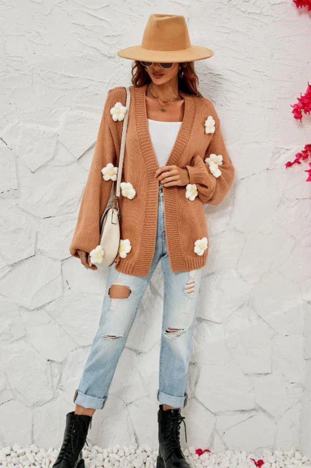 Woman wearing a brown floral cardigan over a white tank top and ripped jeans, accessorized with a hat, sunglasses, and a crossbody bag.