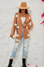Woman wearing a brown floral cardigan over a white tank top and ripped jeans, accessorized with a hat, sunglasses, and a crossbody bag.