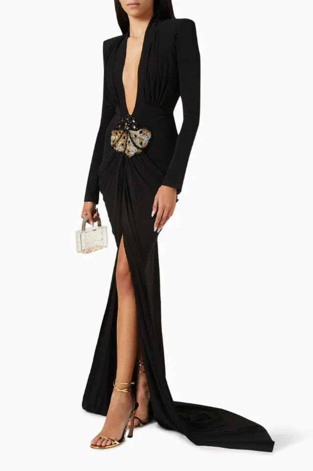 Model posing with a miniature clear clutch, wearing a black draped gown with a high slit and butterfly embellishment.