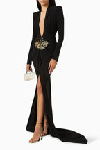 Model posing with a miniature clear clutch, wearing a black draped gown with a high slit and butterfly embellishment.