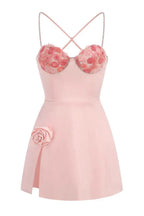 A front view of a pink mini dress with a sweetheart neckline, floral applique, and a high slit.