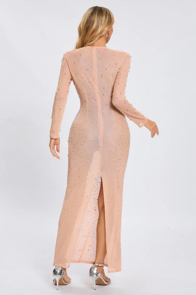 Back view of a woman in a sheer, long-sleeved, full-length gown with a high slit and rhinestone details.