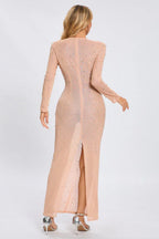 Back view of a woman in a sheer, long-sleeved, full-length gown with a high slit and rhinestone details.