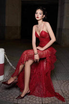 Woman sitting in a red sequined lace evening gown with a high slit and ruffled hem, outdoors at night.