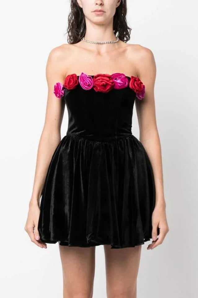 Front view of a woman in a black velvet strapless mini dress with floral trim.