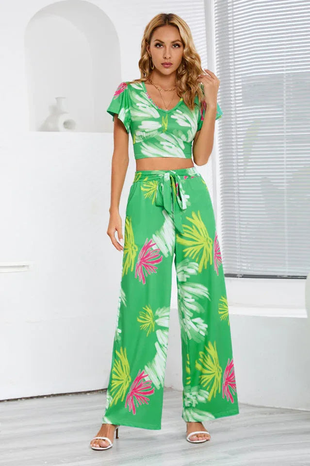 Woman wearing a green floral print two-piece set with a cropped V-neck top and wide-leg pants, front view.